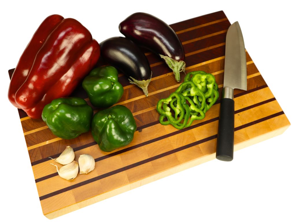 tabla de cocina de madera con pimientos, ajos, berenjenas y un cuchillo
